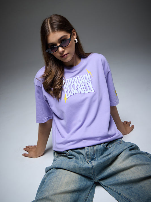 Female model wearing the lavender Joan Alvi Mood Swings oversized T-shirt with Approach Carefully front typography