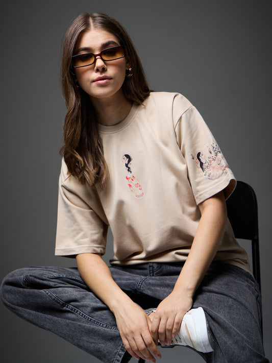 Female model seated in the beige Joan Alvi Smoky Womaniya oversized T-shirt, front view with the small Pataka graphic