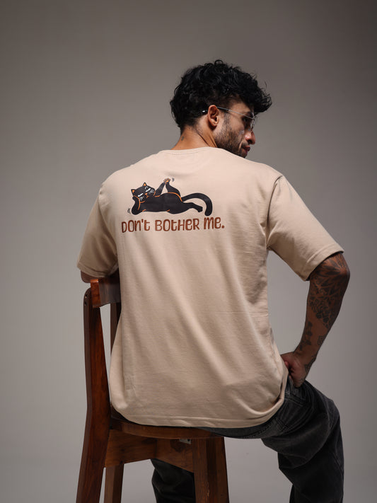 Male model wearing the beige Joan Alvi Morning Mood oversized T-shirt, rear view with the Don't Bother Me cat graphic