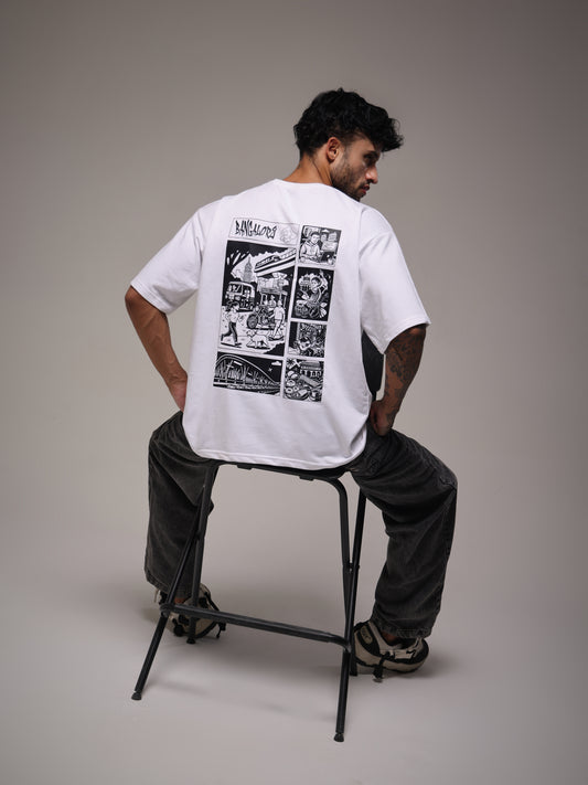 Male model seated in the white Joan Alvi Bangalore oversized T-shirt, rear view with the Bengaluru comic-panel graphic