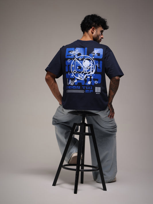 Male model seated in the navy Joan Alvi Lunar Hook oversized T-shirt, showing the astronaut and crescent-moon back graphic